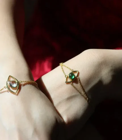 two feminine hands wearing gold bracelets with birthstones in them