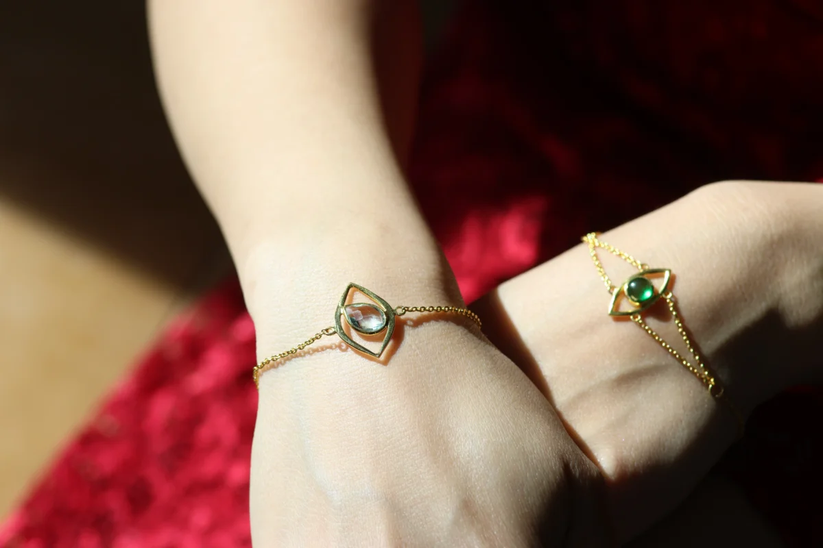 two feminine hands wearing gold bracelets with birthstones in them