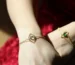 two feminine hands wearing gold bracelets with birthstones in them